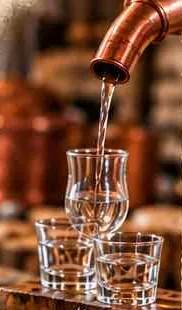 Clear raki poured from a copper spout into small tasting glasses